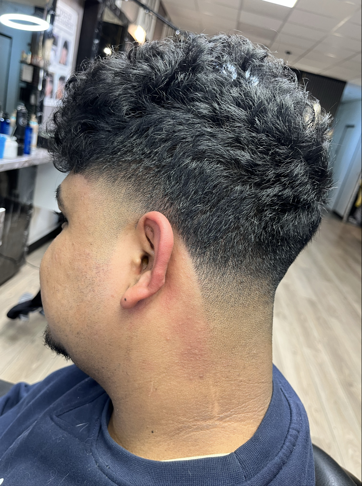 Low fade met krullen bovenop, van opzij en achter gezien